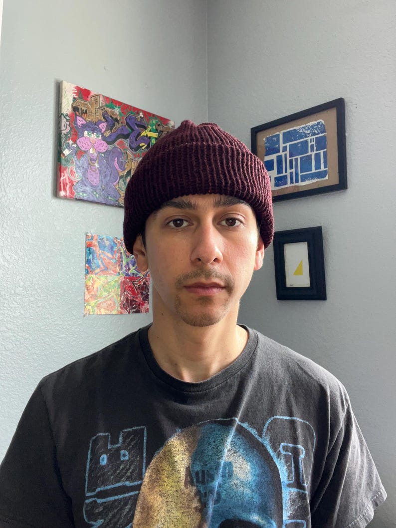 Puede incluir: Un gorro de punto color burdeos oscuro con textura acanalada y borde doblado. El gorro est&aacute; confeccionado con un material de hilo grueso, presentando un patr&oacute;n de puntadas verticales consistente en toda la corona y el borde.