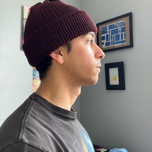 Puede incluir: Un gorro de punto color burdeos oscuro con un borde grueso doblado. El gorro presenta una textura acanalada vertical prominente en toda la superficie, lo que proporciona un ajuste ce&ntilde;ido alrededor de la cabeza. El material es de lana.