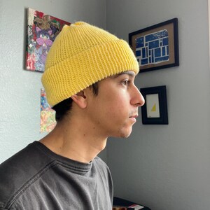 Puede incluir: Un gorro de punto de color amarillo brillante con un borde grueso doblado. El gorro presenta una textura acanalada en toda la tela, proporcionando un patr&oacute;n consistente desde la coronilla hasta el borde. El gorro se lleva sobre la cabeza.