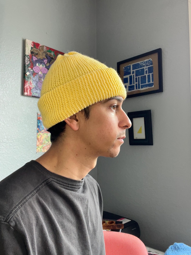 Puede incluir: Un gorro de punto de color amarillo brillante con un borde grueso doblado. El gorro presenta una textura acanalada en toda la tela, proporcionando un patr&oacute;n consistente desde la coronilla hasta el borde. El gorro se lleva sobre la cabeza.