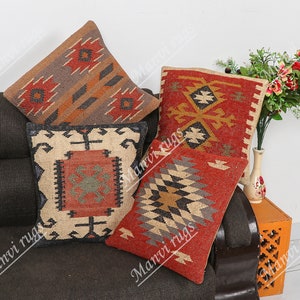 Puede incluir: Cuatro cojines decorativos con patrones geométricos en tonos rojos, marrones, beige y negros. Los cojines están dispuestos en un sofá marrón.