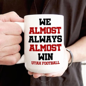 May include: White ceramic coffee mug with black text that reads "We Almost Always Almost Win Utah Football".