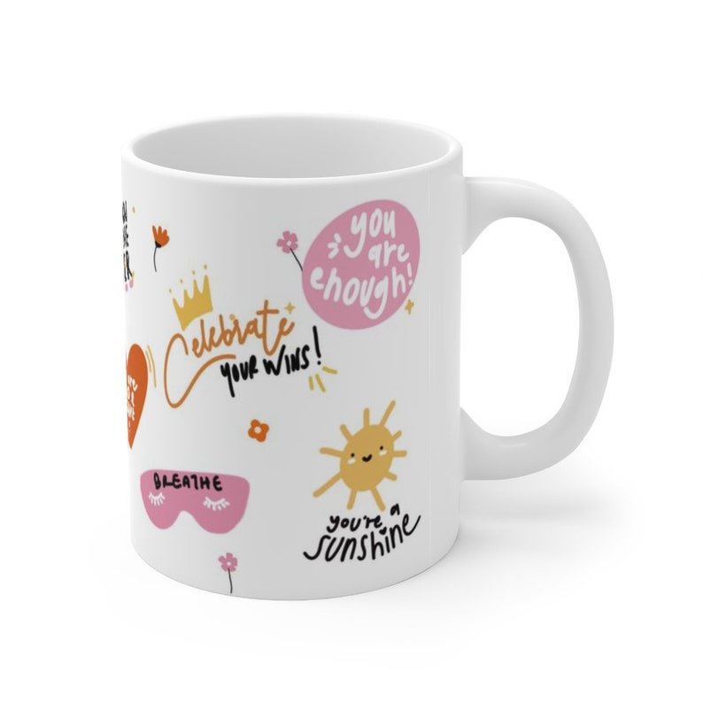 K&ouml;nnte beinhalten: Wei&szlig;e Keramiktasse mit einem farbenfrohen Design mit positiven Affirmationen wie "Du bist genug!" und "Feiere deine Siege!" Die Tasse hat auch eine Sonne mit einem Smiley und den Text "Du bist ein Sonnenschein".