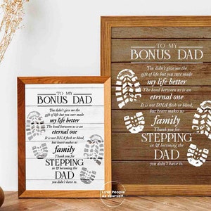 Puede incluir: Dos impresiones enmarcadas con un fondo de madera y texto blanco. El texto dice "To My Bonus Dad" e incluye un poema sobre el v&iacute;nculo entre un padrastro y un hijo. Las impresiones presentan huellas blancas.