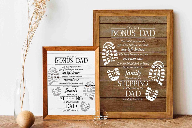 Puede incluir: Dos impresiones enmarcadas con un fondo de madera y texto blanco. El texto dice "To My Bonus Dad" e incluye un poema sobre el v&iacute;nculo entre un padrastro y un hijo. Las impresiones presentan huellas blancas.