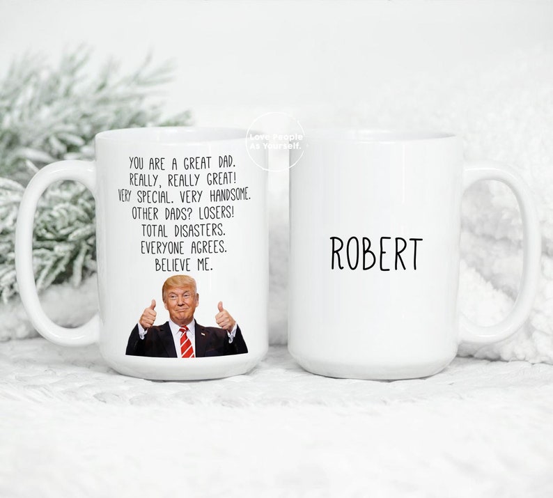 May include: White ceramic coffee mug with a black and white image of a man with a thumbs up gesture. The text on the mug reads "You are a great dad. Really, really great! Very special. Very handsome. Other dads? Losers! Total disasters. Everyone agrees. Believe me." The other side of the mug has the name "Robert" printed on it.