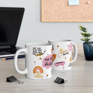 K&ouml;nnte beinhalten: Zwei wei&szlig;e Keramikbecher mit bunten Illustrationen und inspirierenden Zitaten. Ein Becher zeigt einen Regenbogen, eine Wolke mit dem Text "THE MAGIC of SELF-CARE" und den Text "you are worthy". Der andere Becher zeigt eine Sonne, eine Krone und den Text "Celebrate your wins!"