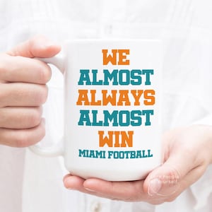 May include: White ceramic coffee mug with the text "We Almost Always Almost Win Miami Football" in orange and teal lettering.