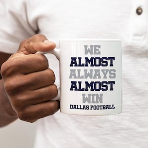 May include: White ceramic coffee mug with the text "We Almost Always Almost Win Dallas Football" in navy blue and gray lettering.