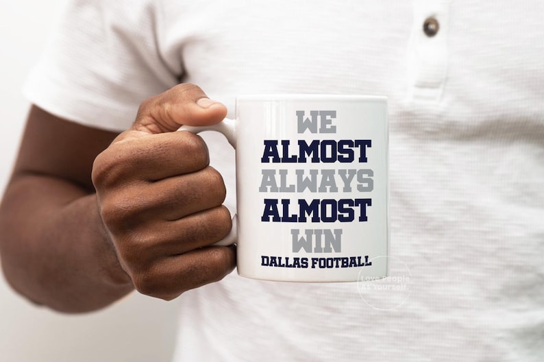May include: White ceramic coffee mug with the text "We Almost Always Almost Win Dallas Football" in navy blue and gray lettering.