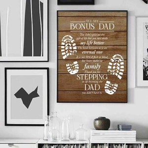 Puede incluir: Un letrero de madera con fondo blanco y textura de veta de madera marr&oacute;n. El letrero dice "To My Bonus Dad" e incluye un mensaje sobre el v&iacute;nculo entre un padrastro y un hijo. El letrero est&aacute; decorado con huellas blancas.