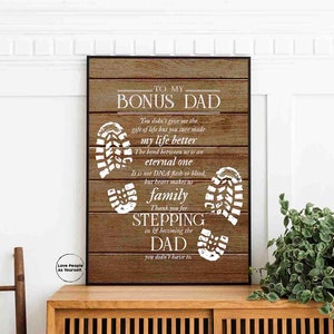 Puede incluir: Un fondo de madera con texto blanco que dice "To My Bonus Dad." El texto contin&uacute;a con un mensaje sobre el v&iacute;nculo entre un padrastro y un hijo. El fondo est&aacute; decorado con huellas blancas.
