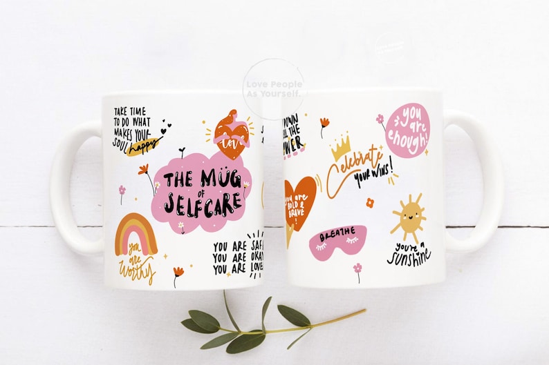 K&ouml;nnte beinhalten: Zwei wei&szlig;e Keramikbecher mit bunten Illustrationen und positiven Affirmationen. Die Becher zeigen S&auml;tze wie "The Mug of Self Care", "You are Worthy", "You are Enough" und "Celebrate Your Wins!"