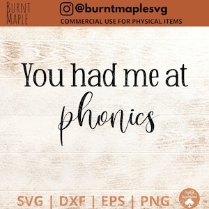 Puede incluir: Una descarga digital de un diseño gráfico con el texto "You had me at phonics" en fuente de letra cursiva negra sobre un fondo de madera blanca.