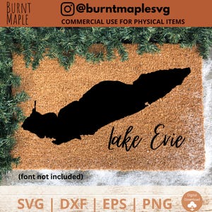 Puede incluir: Una alfombra de bienvenida marr&oacute;n con una silueta negra del lago Evie y el texto "Lake Evie" en una fuente cursiva. La alfombra est&aacute; rodeada de ramas de pino verdes.