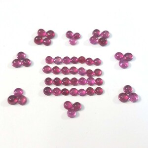 May include: A collection of pink round cabochon gemstones. The gemstones are arranged in a pattern of three, five, and seven stones. The gemstones are all the same size and shape.