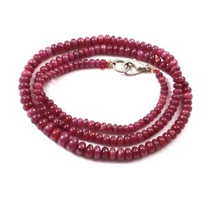 May include: A strand of ruby red beads strung on a silver chain. The beads are round and have a smooth, polished finish.