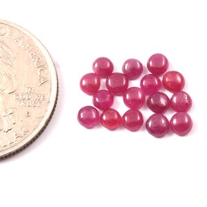 May include: A group of 16 round, red ruby gemstones. The gemstones are approximately the size of a UK 20 pence coin.