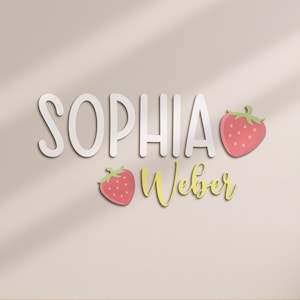 May include: White 3D letters spell "SOPHIA" above "Weber" in yellow script, with two pink strawberries with green stems. The design is set against a neutral background.