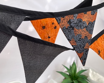 May include: A black and orange Halloween banner with a spiderweb and spider design. The banner is made of fabric and has a black trim.