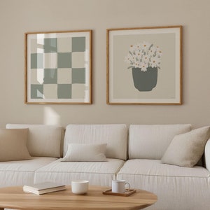 Könnte beinhalten: Ein weißes Sofa mit zwei beigen Kissen und einer weißen Decke. Zwei gerahmte Drucke hängen an der Wand über dem Sofa. Der Druck links ist ein grünes und weißes Karomuster. Der Druck rechts ist eine weiße Blume in einem grünen Topf.