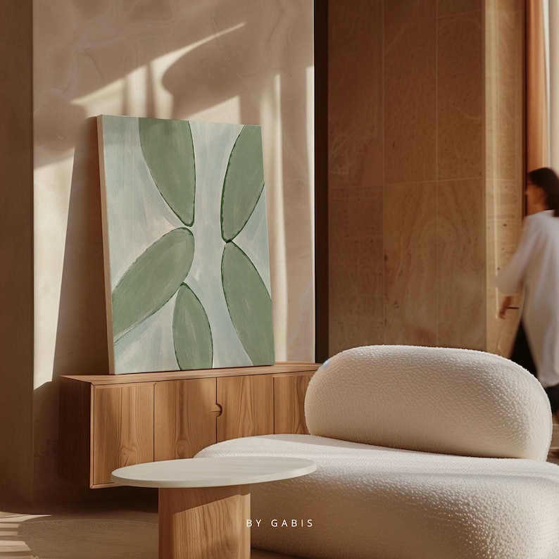May include: A light blue and green abstract painting with a white background hangs on a wall above a wooden cabinet. A white, fluffy, rounded couch sits in front of the cabinet.