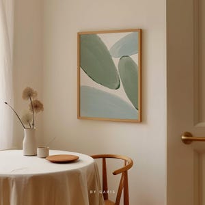 May include: A framed abstract painting with a light blue and green colour scheme. The painting features overlapping organic shapes and is displayed on a white wall.