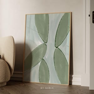 May include: Abstract art print with a light blue background and green leaf shapes. The print is framed in a light wood frame and has the text "BY GABIS" at the bottom.