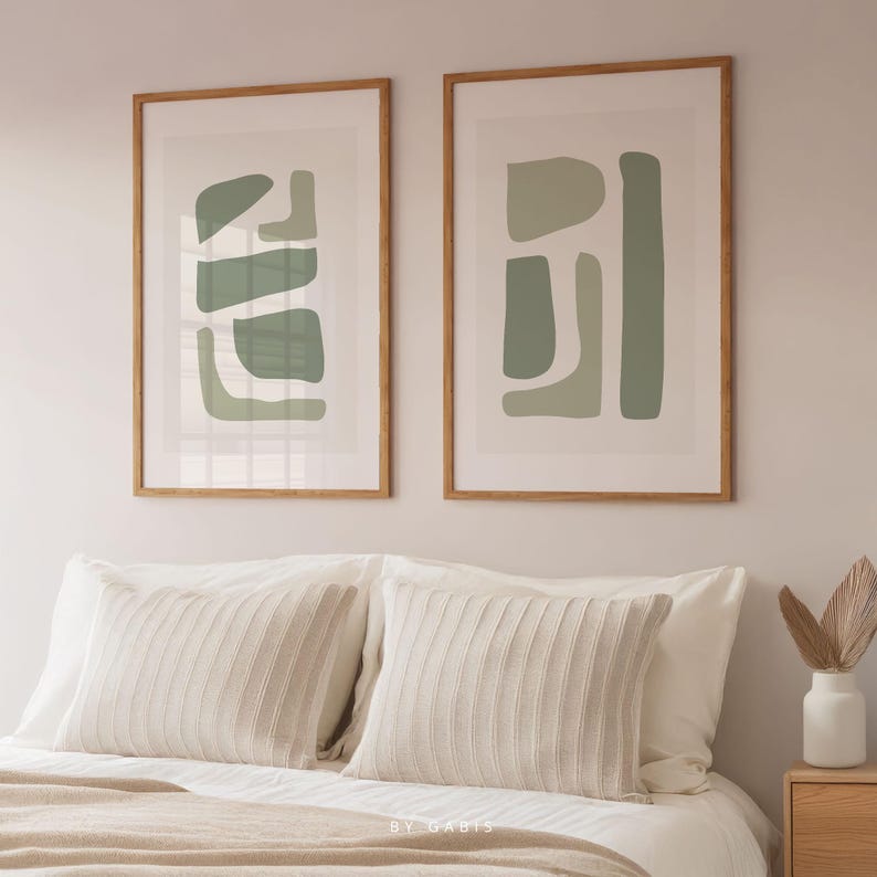May include: Two framed abstract art prints with a green and white color scheme. The prints are hung on a white wall above a bed with white bedding and a beige throw blanket.