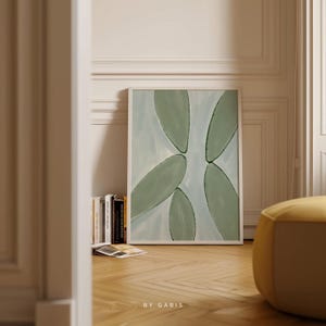 May include: A framed abstract art print with a white frame and a light blue background with green leaf shapes. The print is titled "By Gabis".