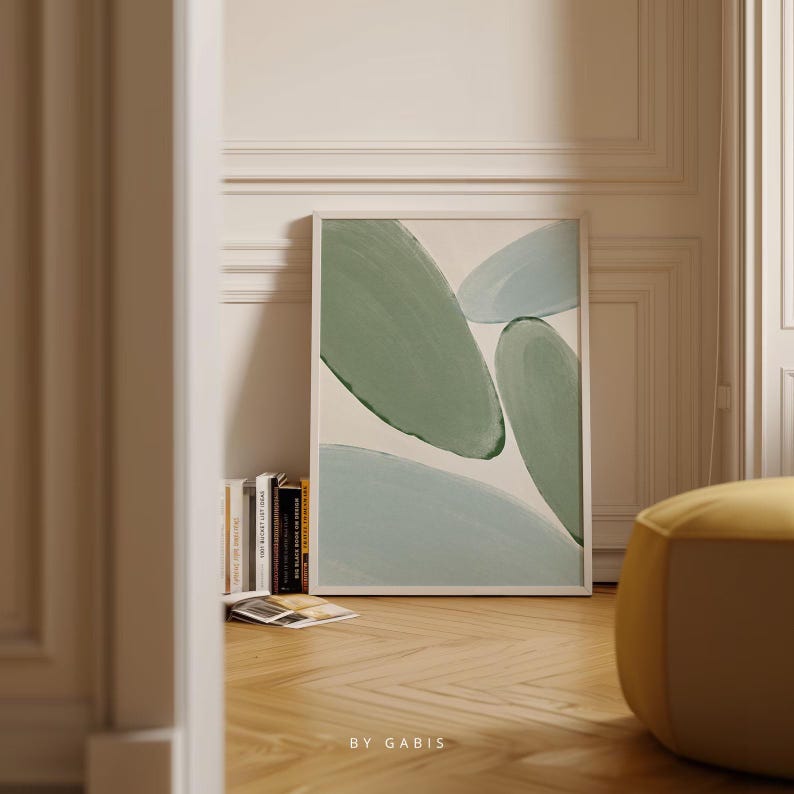 May include: Abstract art print featuring green and blue shapes on a white background. The print is framed and displayed on a white wall.