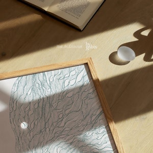 May include: A framed print of a blue and white abstract design. The design resembles a stylized tree with branches and leaves. The print is in a light wood frame and is sitting on a wooden surface. The text "Shop the Collection by gabis" is visible below the print.