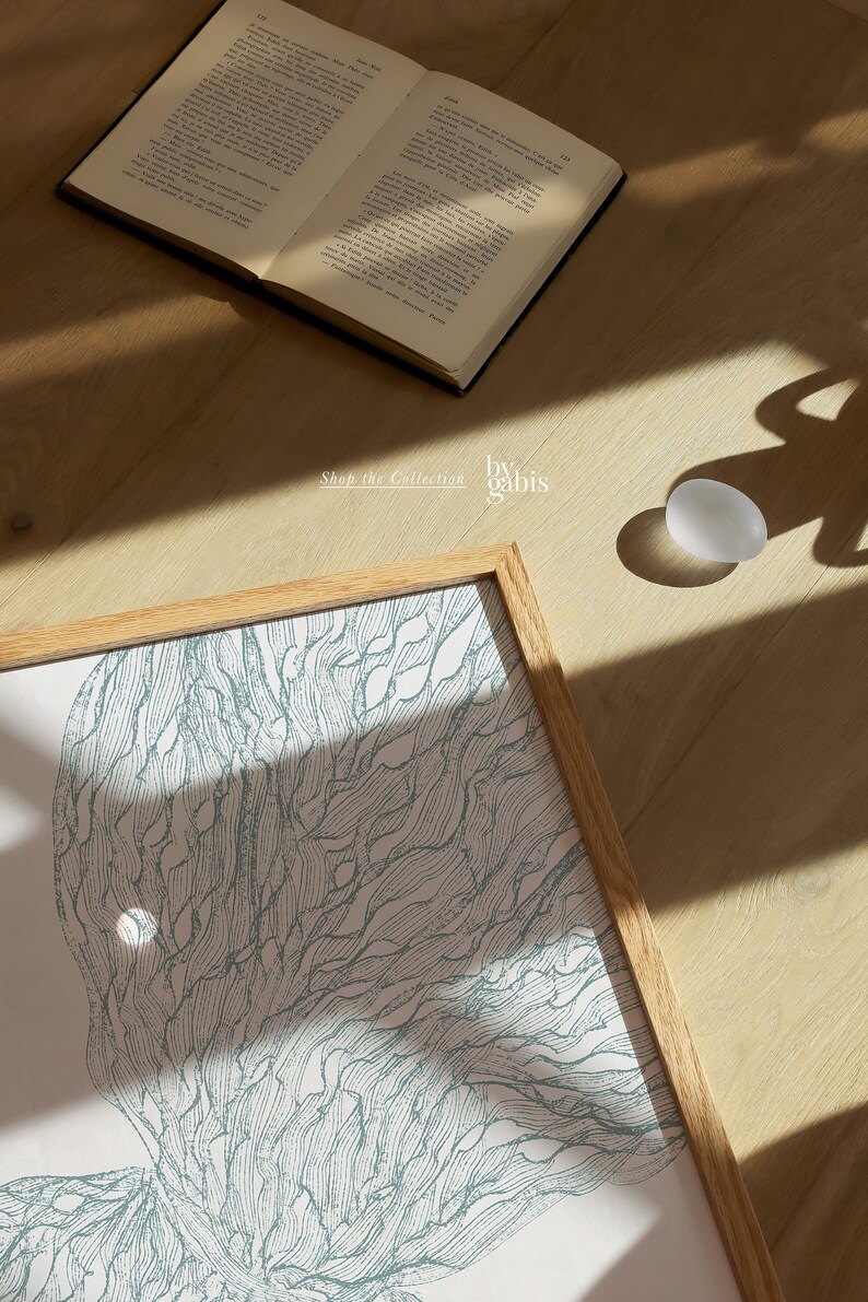 May include: A framed print of a blue and white abstract design. The design resembles a stylized tree with branches and leaves. The print is in a light wood frame and is sitting on a wooden surface. The text "Shop the Collection by gabis" is visible below the print.