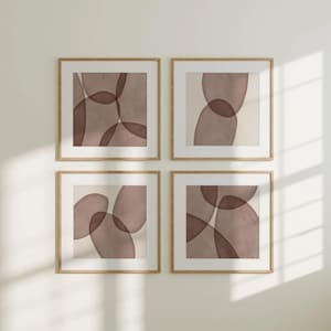 May include: Four framed abstract art prints. Each square frame features a beige background with overlapping, organic shapes in shades of brown. The frames are a light wood colour, and the artwork is displayed on a white wall.