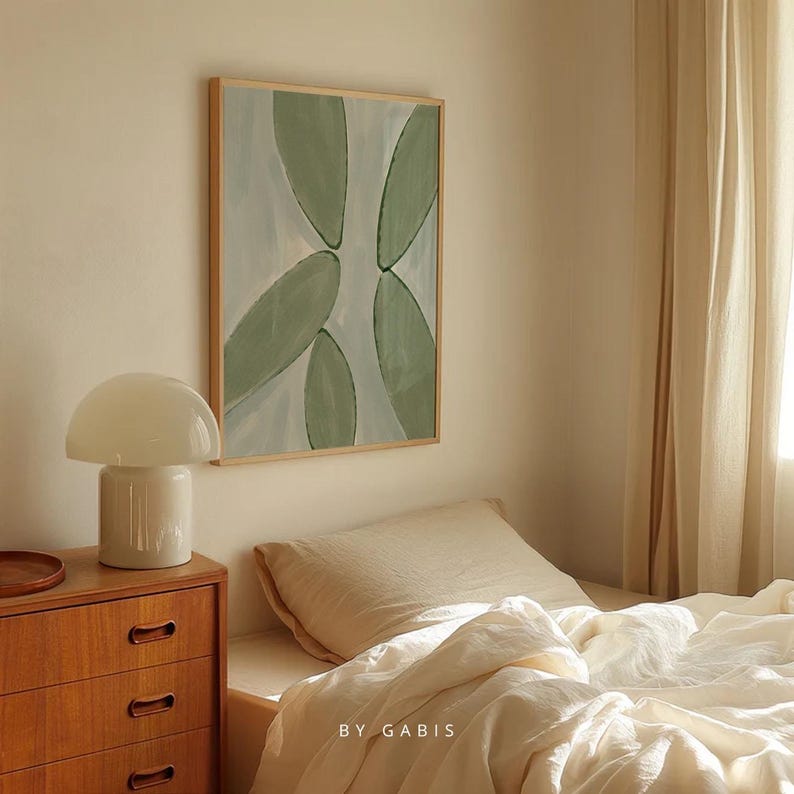 May include: A framed abstract painting with green and blue shapes on a white background. The painting is hanging on a wall in a bedroom with a white lamp and a bed with white bedding.