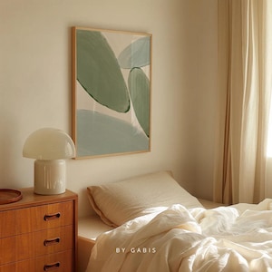 May include: A bedroom interior featuring a white lamp on a wooden chest of drawers, a bed with white linen bedding and a beige pillow, and a framed abstract painting with green and blue shapes on the wall. The text "BY GABIS" is visible on the bed linen.