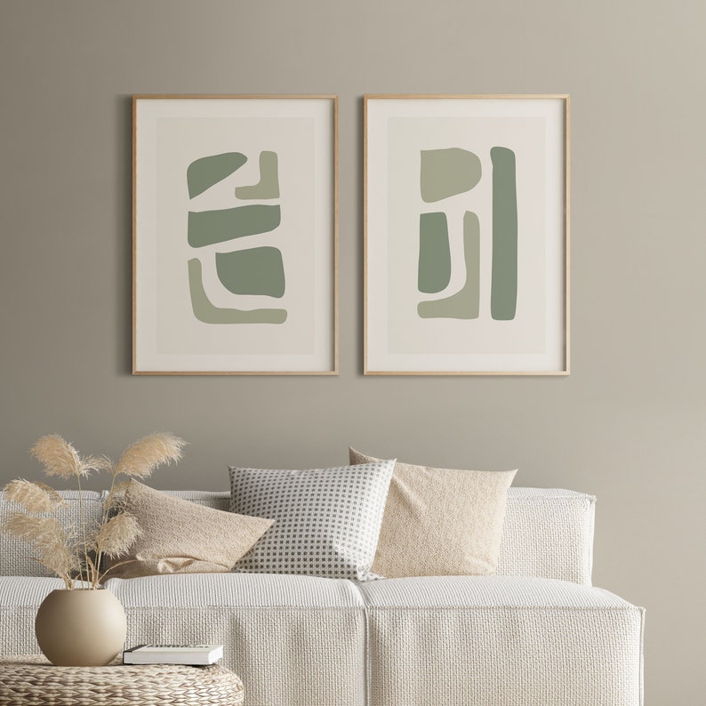 May include: Two framed abstract art prints with a light green and white color scheme. The prints are hanging on a light beige wall above a white couch with beige and white patterned pillows.