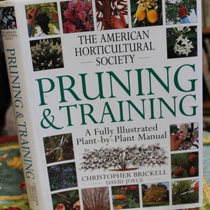 May include: A hardcover book titled "Pruning & Training" by The American Horticultural Society. The cover features a green title and various plant illustrations. The book is a plant-by-plant manual.
