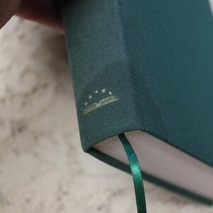 May include: A dark green hardcover book with a gold ribbon bookmark. The book has a gold embossed design on the cover that includes a book and five stars.