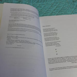 May include: An open book with white pages, featuring text on both sides. The left page displays copyright information and details, while the right page presents a poem titled "The Stones." The book is held open by a hand.