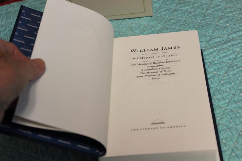May include: A hardcover book titled William James Writings 1902-1910, featuring a white title page with black text listing works including The Varieties of Religious Experience, Pragmatism, A Pluralistic Universe, The Meaning of Truth, and Some Problems of Philosophy.