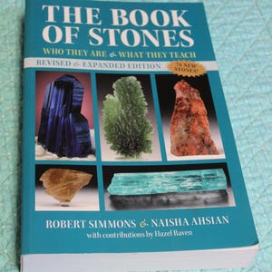 May include: A book titled "THE BOOK OF STONES" with a teal cover. The cover features images of various stones and the text "WHO THEY ARE & WHAT THEY TEACH" and "REVISED & EXPANDED EDITION". Authors are Robert Simmons and Naisha Ahsian.