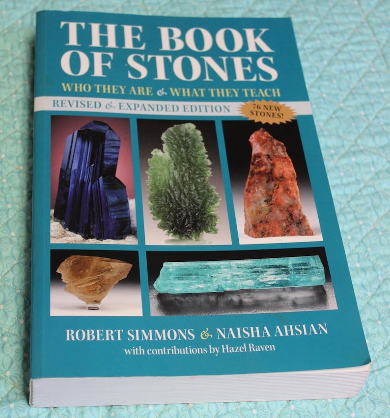 May include: A book titled "THE BOOK OF STONES" with a teal cover. The cover features images of various stones and the text "WHO THEY ARE & WHAT THEY TEACH" and "REVISED & EXPANDED EDITION". Authors are Robert Simmons and Naisha Ahsian.