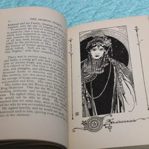 May include: Open book with text and an illustration of a woman in a decorative frame. The illustration is black and white and features a woman with a detailed headdress and jewelry. The text reads "The Arabian Nights."