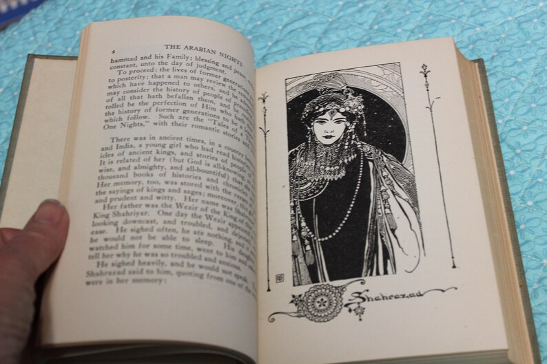 May include: Open book with text and an illustration of a woman in a decorative frame. The illustration is black and white and features a woman with a detailed headdress and jewelry. The text reads "The Arabian Nights."