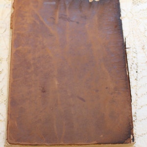 May include: A brown leather-bound book with a worn and aged appearance. The cover is smooth and has a slightly textured surface.