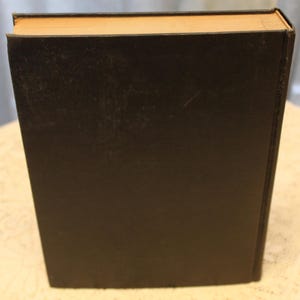 May include: A black hardcover book with a tan spine.