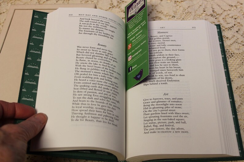 May include: An open book with green pages and a green bookmark. The book is titled "May-Day and Other Pieces" and contains poems about beauty, manners, and art. The bookmark has the word "FRIENDS" printed on it.