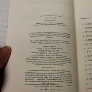 May include: A book titled "Black Holes and Baby Universes" by Stephen Hawking. The book cover features a black and white illustration of a swirling galaxy with stars. The book was published by Bantam Books in 1993.