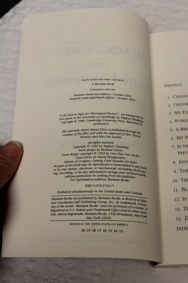 May include: A book titled "Black Holes and Baby Universes" by Stephen Hawking. The book cover features a black and white illustration of a swirling galaxy with stars. The book was published by Bantam Books in 1993.